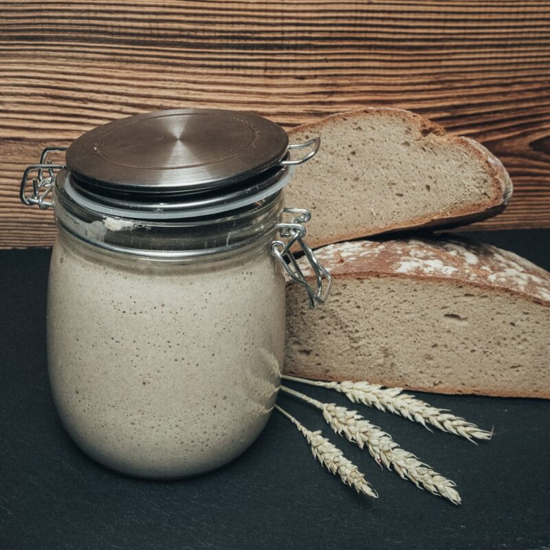 Aktiver Sauerteig im Glas vor aufgeschnittenem Brot