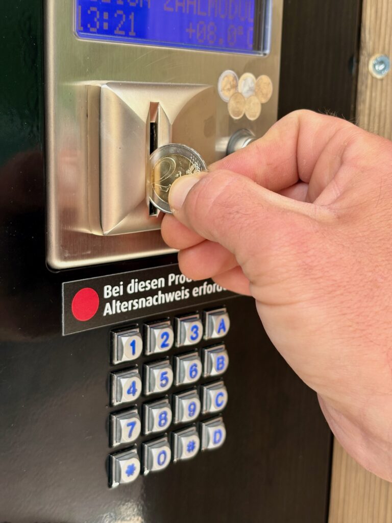Hand wirft eine Münze in den Genussautomaten beim Das Eggen ein