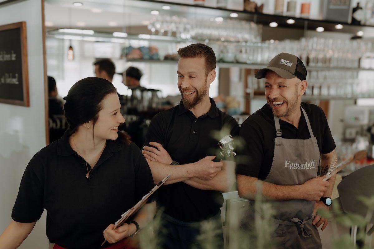 Drei lachende Teammitglieder hinter der Bar im Eggen - Café Bistro, bereit für den Service.