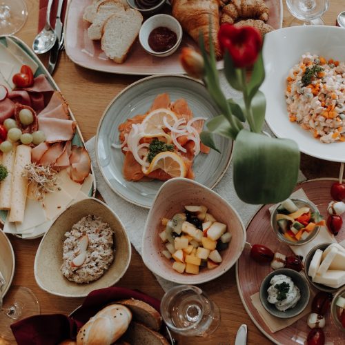 Frühstückstisch im Eggen - Café Bistro mit regionalen Spezialitäten, Käseplatte, frischem Brot, Obstsalat und Croissants, liebevoll angerichtet auf Holztisch.